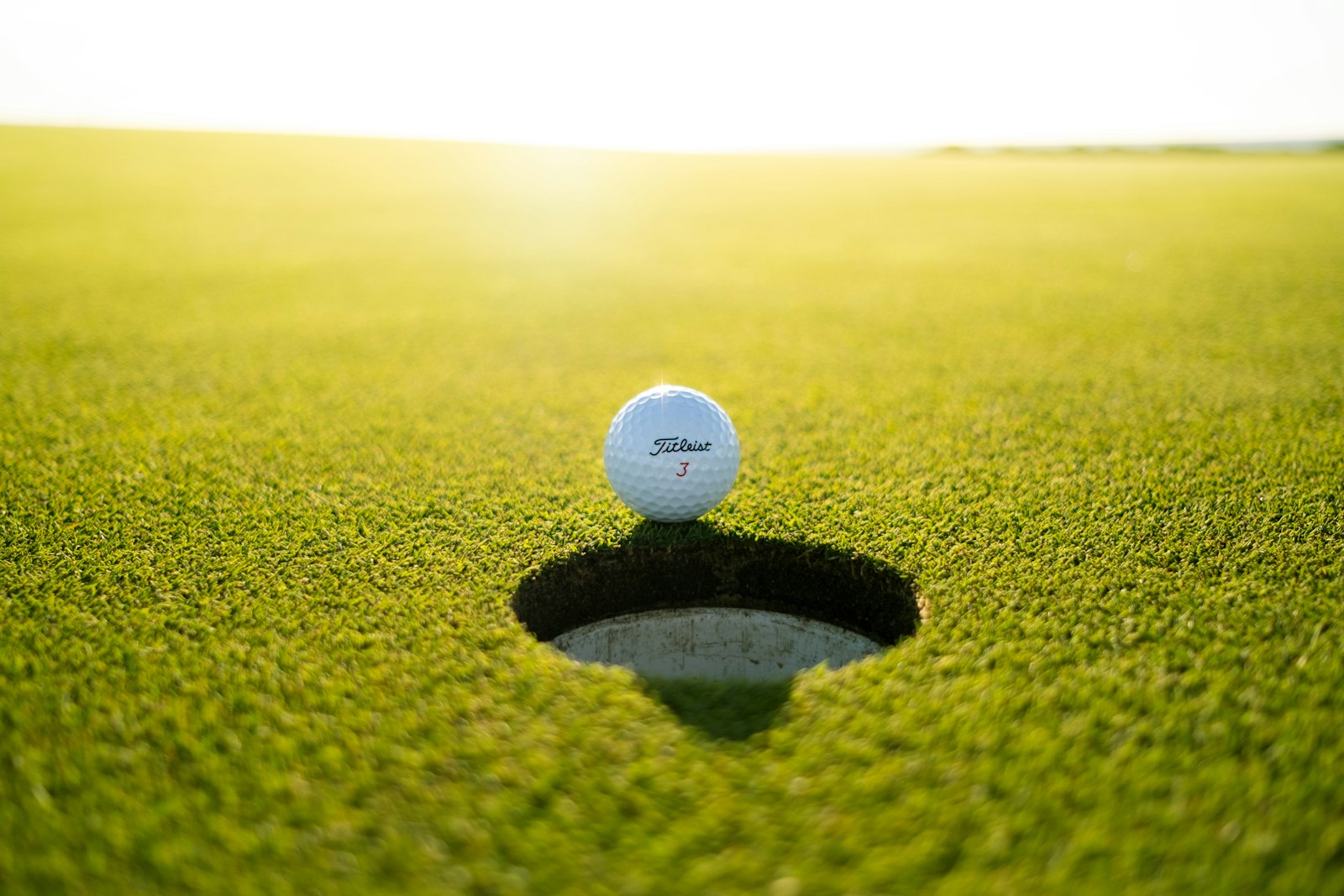 Golf ball at the edge of the cup on a sunlit green