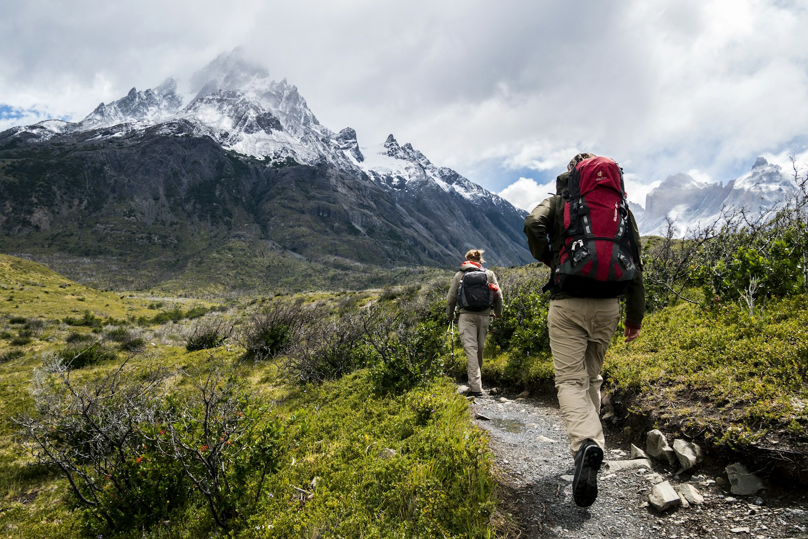 Two hikers on a trail toward snow-capped peaks